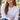 Woman in a white long-sleeve top wearing the gold evil eye pendant necklace, seated outdoors