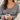 Woman wearing the gold Shira Necklace with a grey V-neck sweater, holding a cup of tea