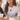 Smiling woman wearing the gold enamel charm medallion necklace with a white tee at a cafe with friends